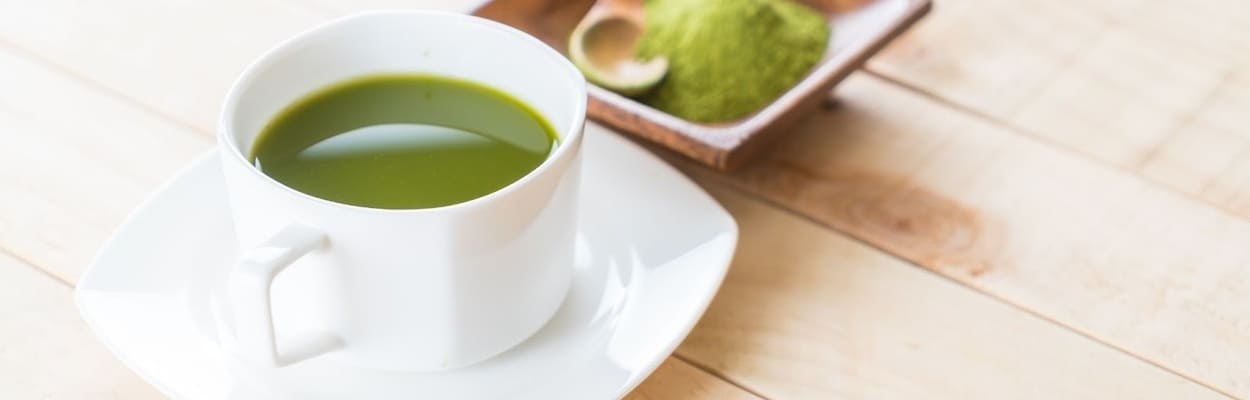 Imagem mostrando o que é matcha, com uma xícara de chá verde e um recipiente de madeira preenchido pelo pó da bebida.