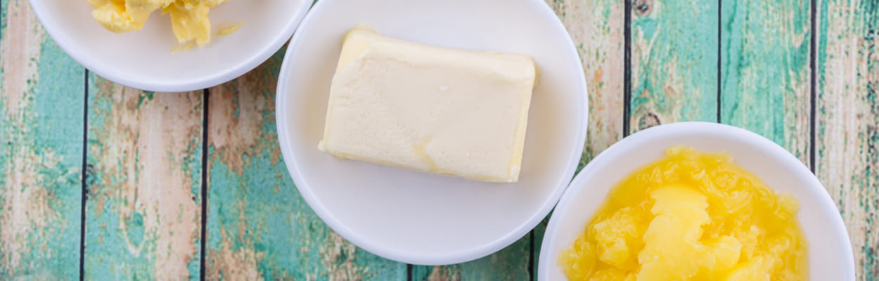 Margarina ou manteiga? Três pratos brancos sobre uma superfície de madeira rústica azul com as opções