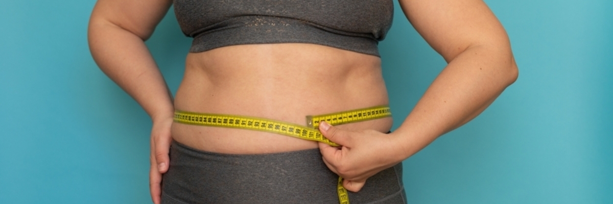 Mulher com roupas de academia medindo com uma fita métrica sua circunferência abdominal, onde fica localizada a gordura visceral.