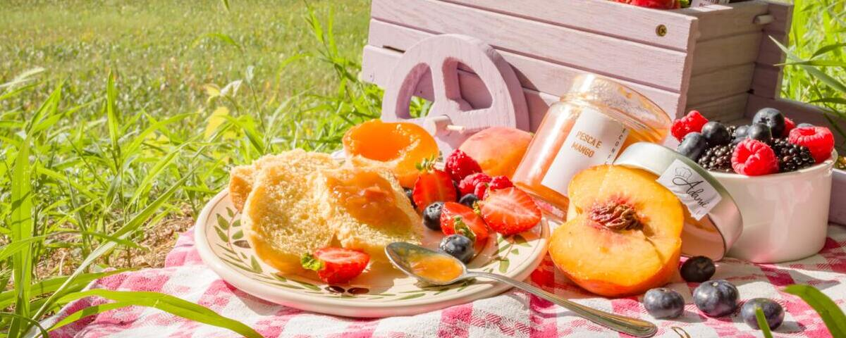 Toalha de piquenique posta num campo ensolarado com pêssegos, morangos, e potes de geleia.