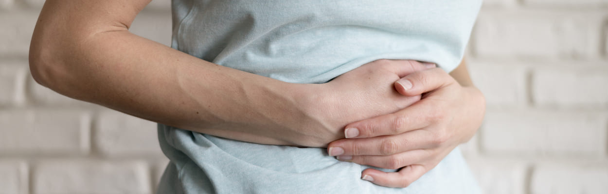 Mulher com as duas mãos sobre a barriga em sinal de dor. A imagem representa qual a diferença entre intoxicação e infecção alimentar.