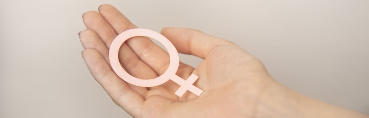 Mão de uma mulher segurando um símbolo do gênero feminino feito de papel. A imagem representa o desequilíbrio hormonal feminino.