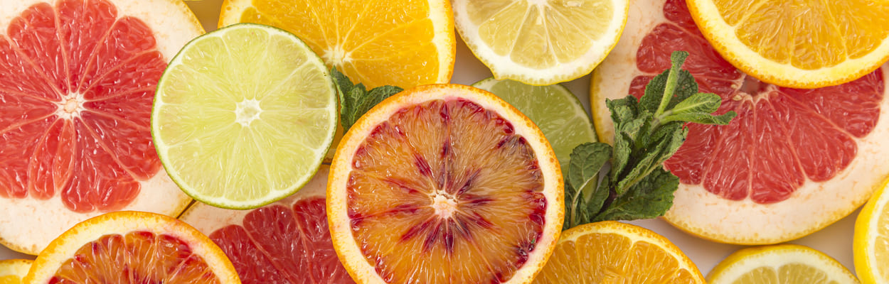Frutas cítricas variadas cortadas ao meio, como o limão e a laranja. A imagem representa os alimentos ricos em citrato.