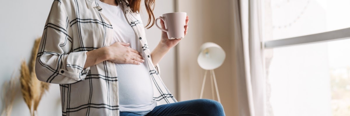 Respondendo se grávida pode tomar chá, uma gestante está sentada com uma mão na barriga e a outra segurando uma xícara.