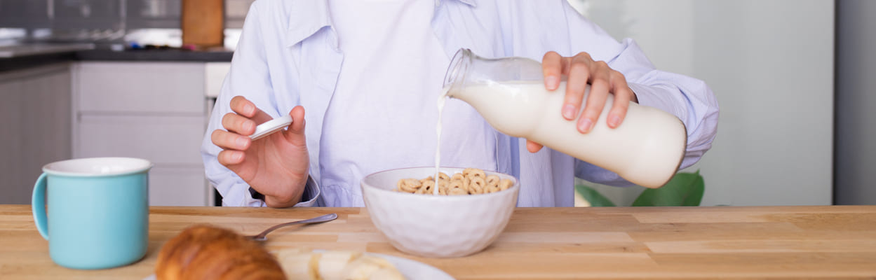 Mulher sorrindo enquanto despeja leite zero lactose em uma tigela com cereal. A imagem representa se quem tem intolerância à lactose pode tomar leite zero lactose.