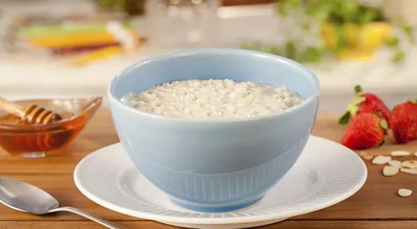  Em cima de um prato branco, há uma cumbuca azul clara com mingau de aveia.