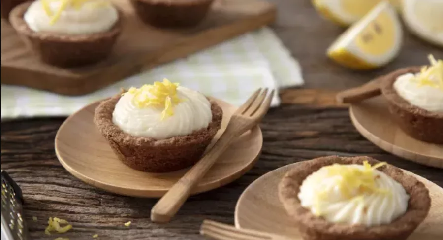 Mini tortas de limão saudável em cima de pratinhos de madeira, onde cada um possui um garfo pequeno.