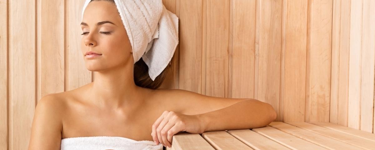 Mulher vestindo toalha no corpo e na cabeça aproveitando os benefícios da sauna.