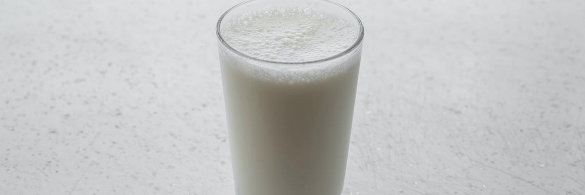 Numa superfície branca, um copo transparente de leite cheio pela boca.