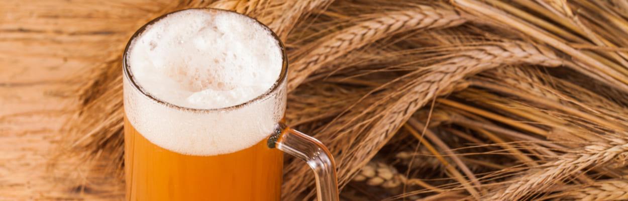 Copo de cerveja maltada, ramos de trigo e cereais de cevada sobre uma mesa de madeira, representando a levedura de cerveja.