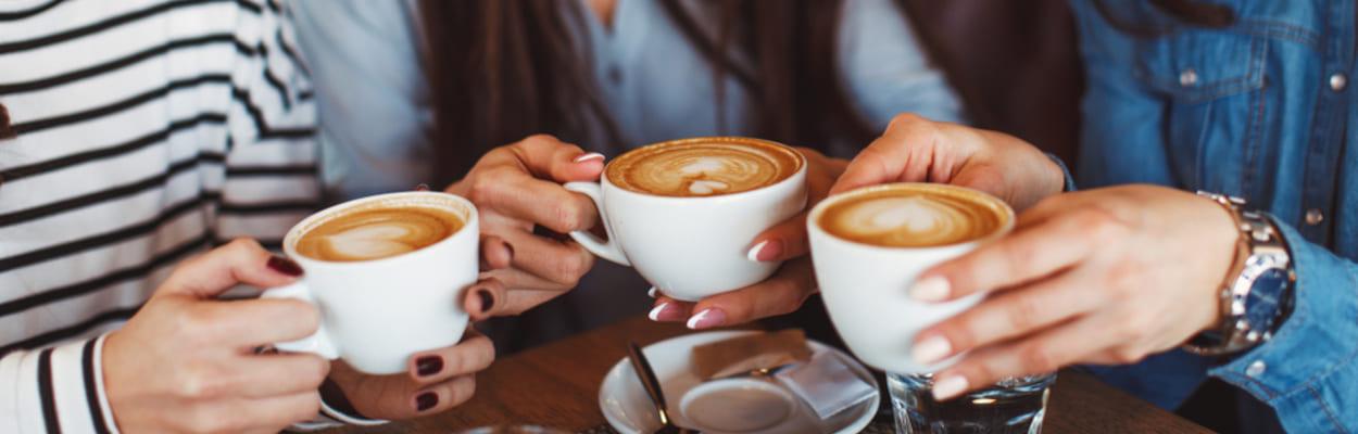 Para falar sobre os benefícios do café, uma foto de três mulheres adultas conversando, rindo e segurando xícaras de café.