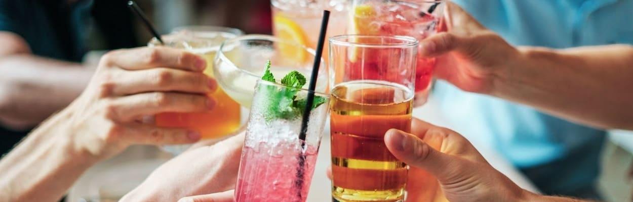  Foto de mãos segurando drinks sem álcool, coloridos e se encontrando acima da mesa para um brinde.