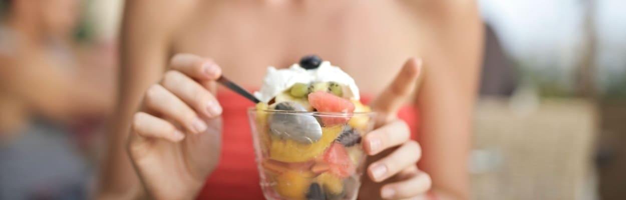 Mulher sentada à mesa, comendo de uma taça com frutas diversas para um melhor equilíbrio digestivo.