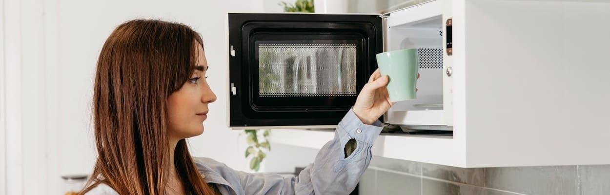 mulher em uma cozinha colocando uma xícara em um micro-ondas.