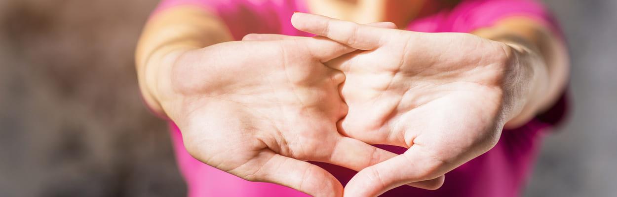 mulher com camiseta rosa alongando seus braços enquanto estala os dedos das mãos. A imagem representa a pergunta se estalar os dedos faz mal.