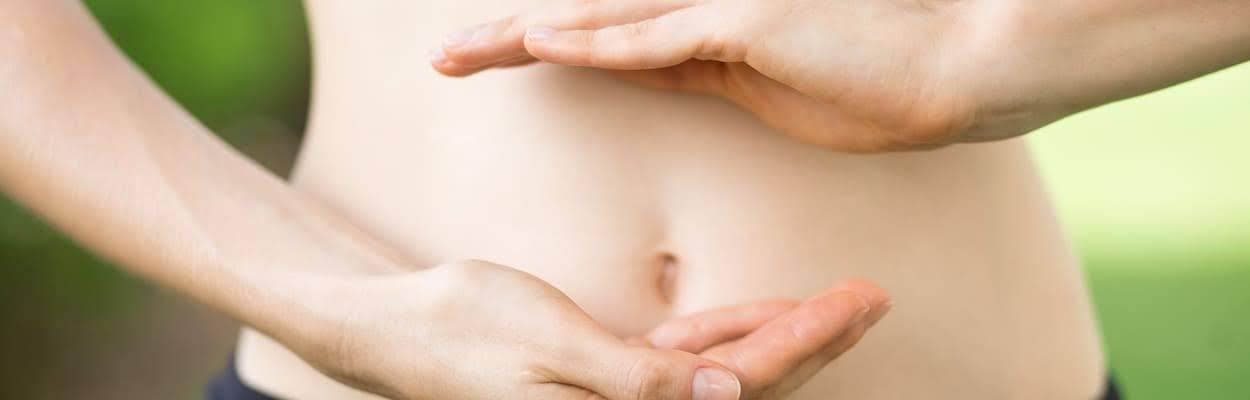 Duas mãos de uma mulher na frente da barriga, sinalizando o intestino. A imagem representa o que é modulação intestinal.