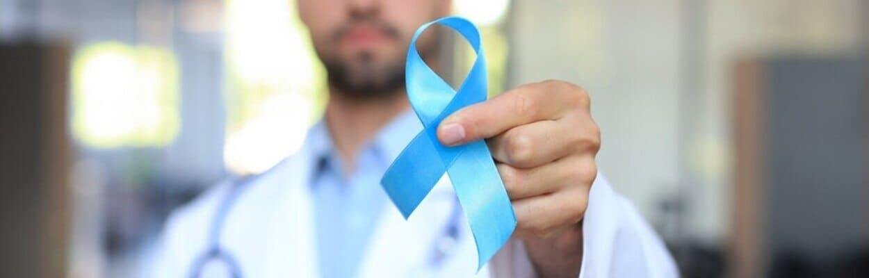 Médico com jaleco e estetoscópio segurando um laço azul com a mão, simbolizando o novembro azul e como prevenir o câncer de próstata. 