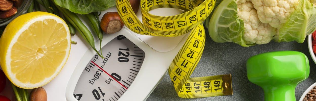 Balança digital com frutas e legumes em cima, junto a uma fita métrica. A imagem representa a dieta do tipo sanguíneo.